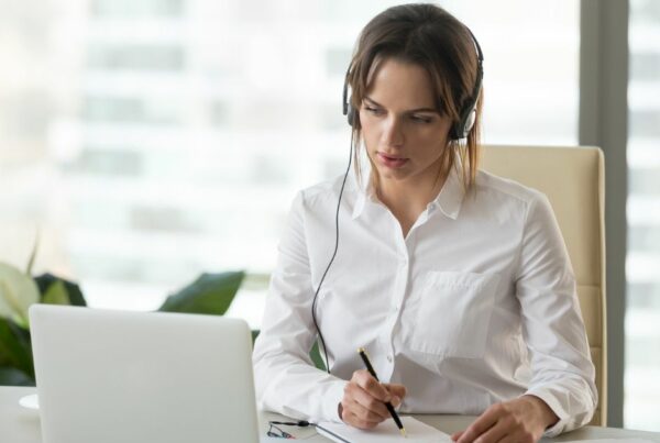 Woman with headphone looking at laptop screen and writing on a notebook